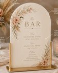 Decorative bar sign with floral design and gold stand on a table setting.