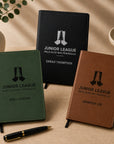 Three personalized notebooks with 'Junior League' branding on a wooden surface.