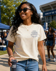 Woman wearing a beige t-shirt with 'JSU' on it, holding a cup, and standing in a casual outdoor setting.