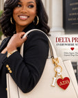Stylish Black woman carrying a cream handbag featuring the Delta Sigma Theta I Heart DST enamel bag charm
