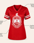 Red short-sleeve athletic V-neck jersey with white sleeve stripes and a large white crest graphic on the front, shown on a light beige background with callout labels describing features.