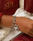 Close-up of Delta Sigma Theta pyramid charm bracelet worn on wrist with matching sorority accessories in crimson and gold.