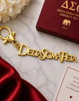 Officially licensed Delta Sigma Theta script logo keychain in a polished gold finish with lobster clasp displayed on a marble surface with luxury gift packaging and elegant red satin accents.