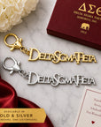 Officially licensed Delta Sigma Theta script logo keychain available in polished gold and silver finishes displayed side by side on a luxury marble flat lay.
