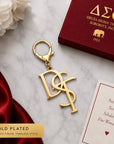 Delta Sigma Theta DST monogram gold keychain with lobster clasp on marble surface next to crimson gift box