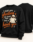A black crewneck sweatshirt shown from both front and back. The front features a graphic design with the text 'I told you ghosting me would come back to haunt you' in white and orange lettering, alongside an illustration of a cartoon ghost wearing sunglasses and making a peace sign.