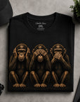 Folded black graphic t-shirt with detailed three wise monkeys artwork displayed in flat lay setup