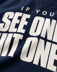 Close-up of a navy blue sweatshirt featuring bold white text that reads 'IF YOU SEE ONE, HIT ONE.'