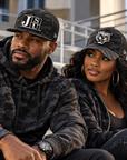 Black man and woman modeling Jackson State Black Camo New Era 9FIFTY and 39THIRTY patch hats