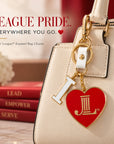 Junior League I Heart JL enamel bag charm attached to a cream handbag with gold-tone hardware