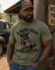 Man wearing olive green A Hard Head Makes a Soft Ass graphic t-shirt styled with western workwear clothing