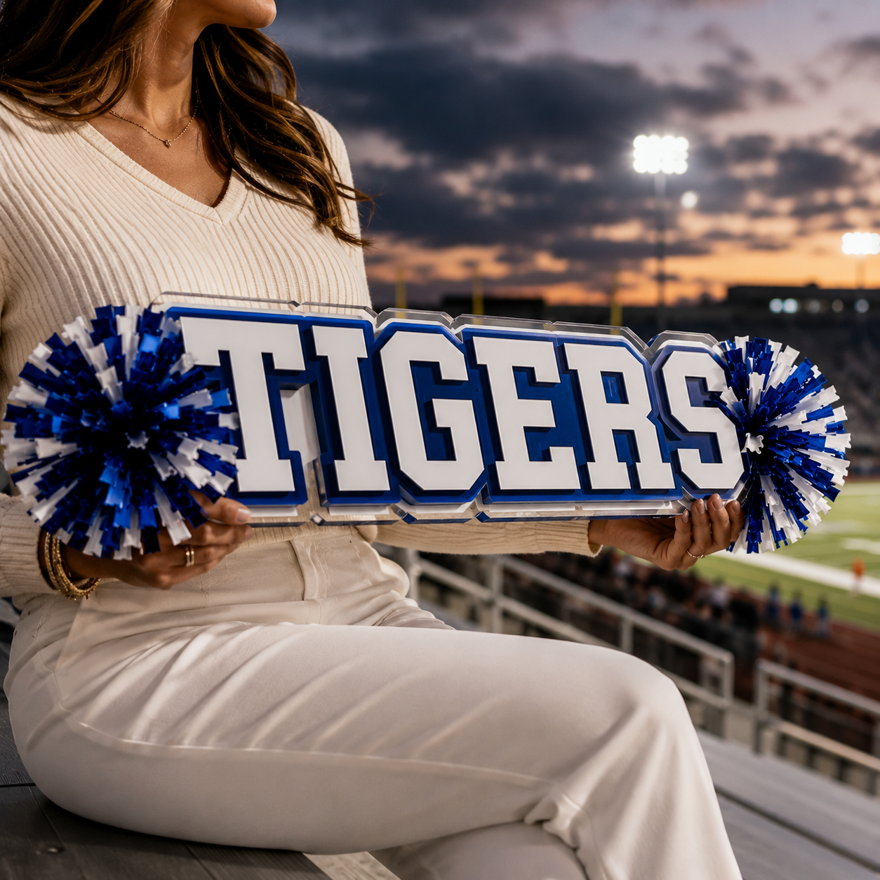 Person holding an acrylic spirit stick with blue and white lettering and pom-poms