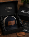 Navy blue cap with leather patch in a black box, surrounded by 'coleman winz' branded items on a wooden surface.