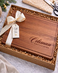Wooden cutting board with engraved name in a gift box with ribbon and tag.
