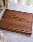 Wooden cutting board with 'Johnson EST. 1983' engraving on a marble countertop.