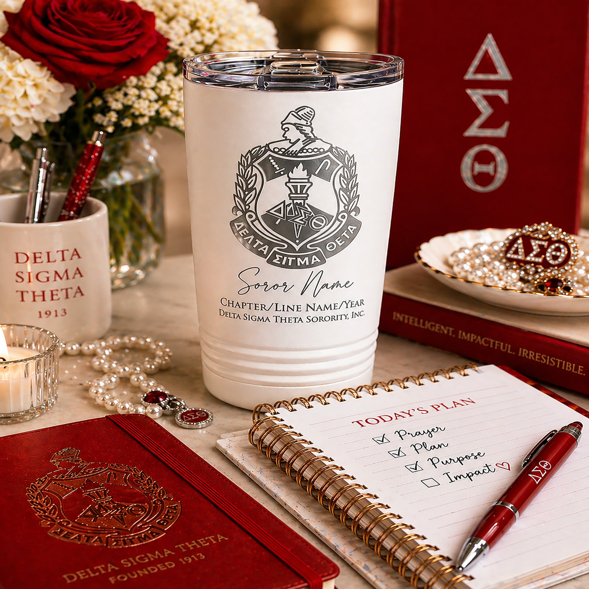 White tumbler with Delta Sigma Theta sorority emblem and name on a table with books and stationery.