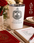 White tumbler with Delta Sigma Theta sorority emblem and name on a table with books and stationery.