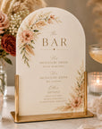 Decorative bar sign with floral design on a table with candles and cocktails.