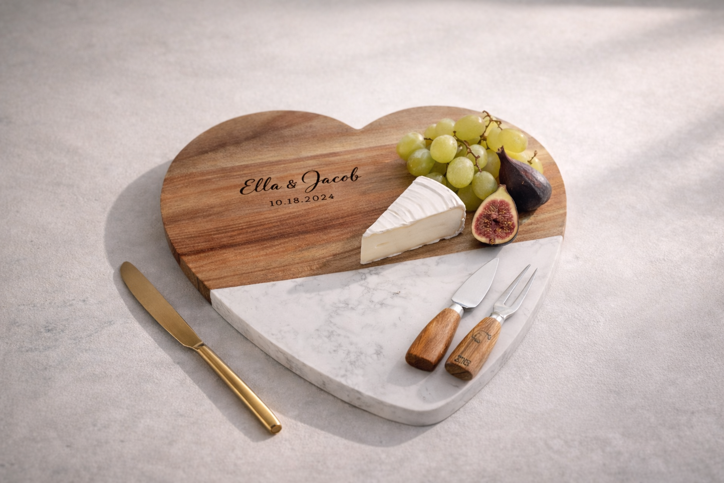 Heart-shaped marble and wood cutting board with cheese, grapes, and figs on a light gray background.