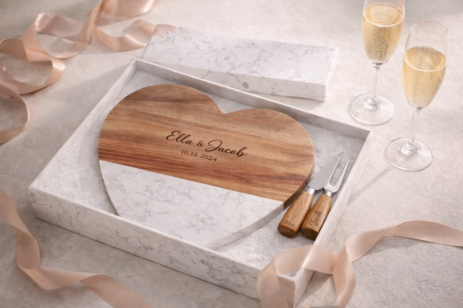 Heart-shaped cutting board with engraved names and date, accompanied by a knife and fork set, on a light gray surface with ribbons and champagne glasses.