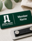 Laser engraved green and white two-tone acrylic Junior League Palo Alto Mid Peninsula custom member name badge with magnetic back shown on linen surface with eucalyptus leaves