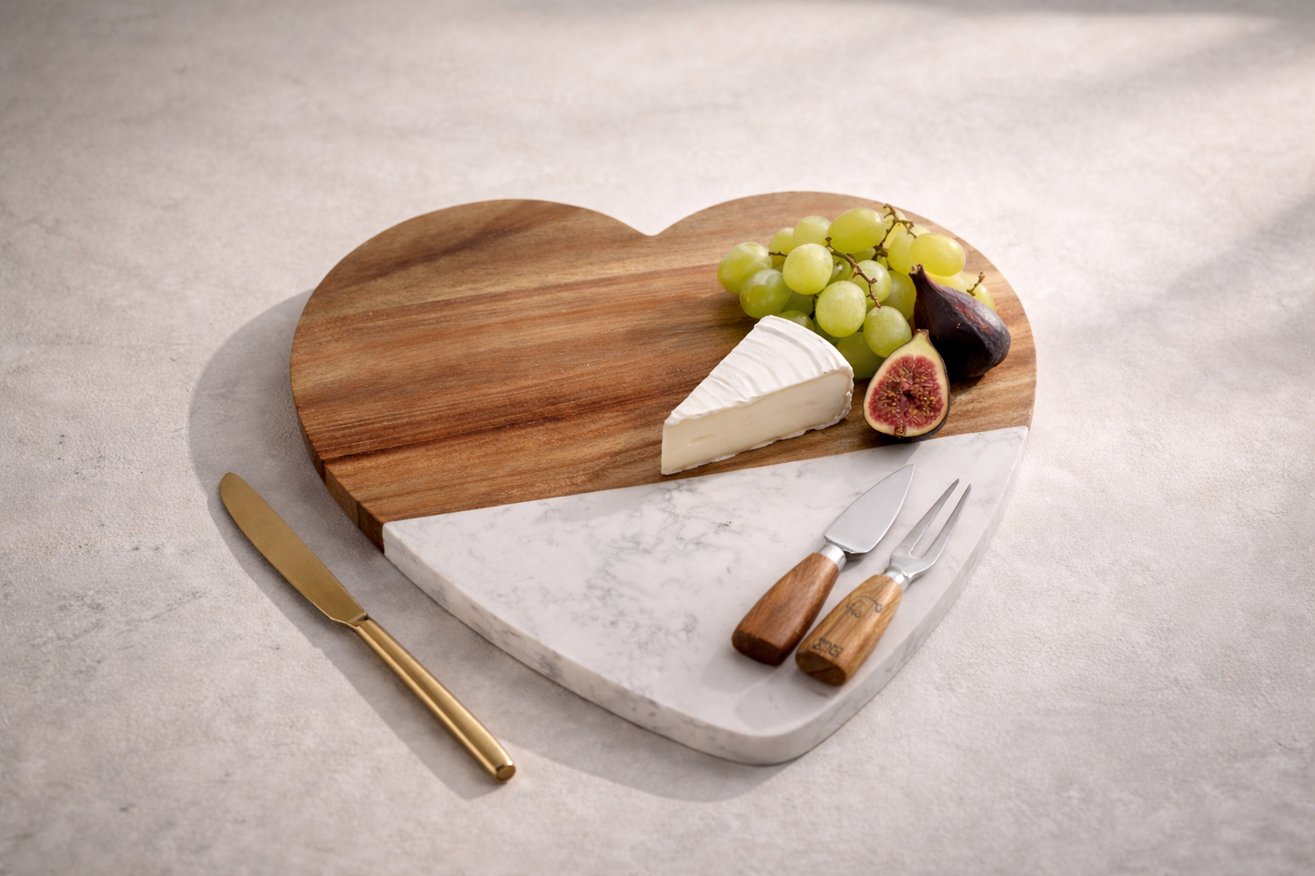 Heart-shaped cutting board with cheese, grapes, figs, and knives on a light surface