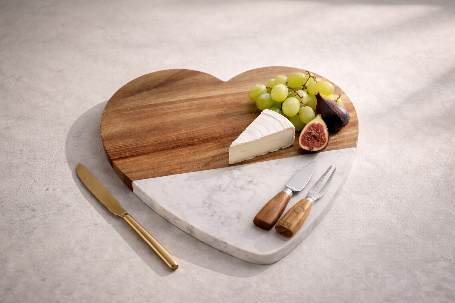 Heart-shaped cutting board with cheese, grapes, figs, and knives on a light surface