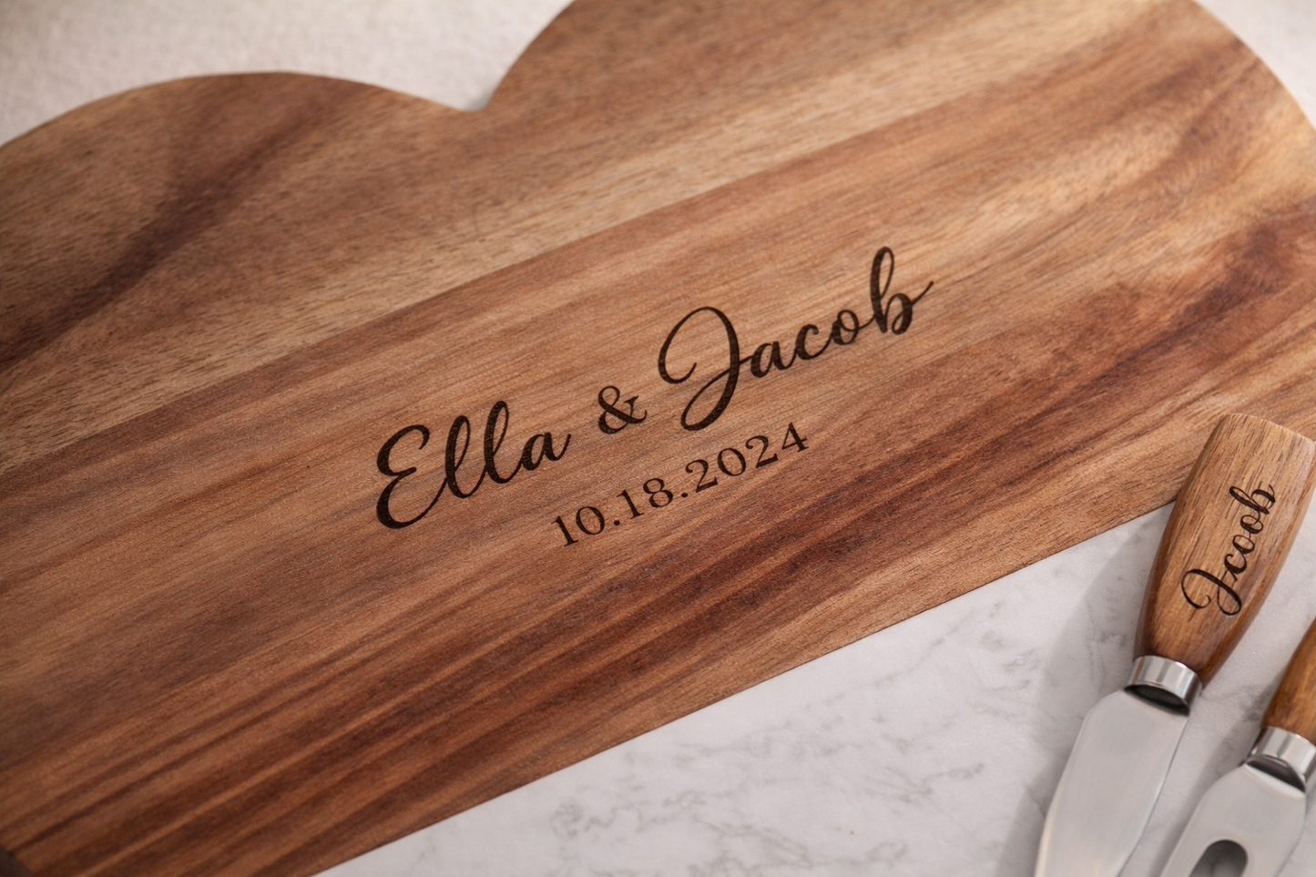 Wooden cutting board with engraved names and date, accompanied by a knife and cheese knife.