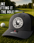 Dark gray trucker golf hat with black mesh sides and circular 'I Like Putting In The Hole' patch