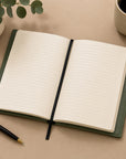 Open notebook with lined pages on a beige surface, accompanied by a pen and a cup.