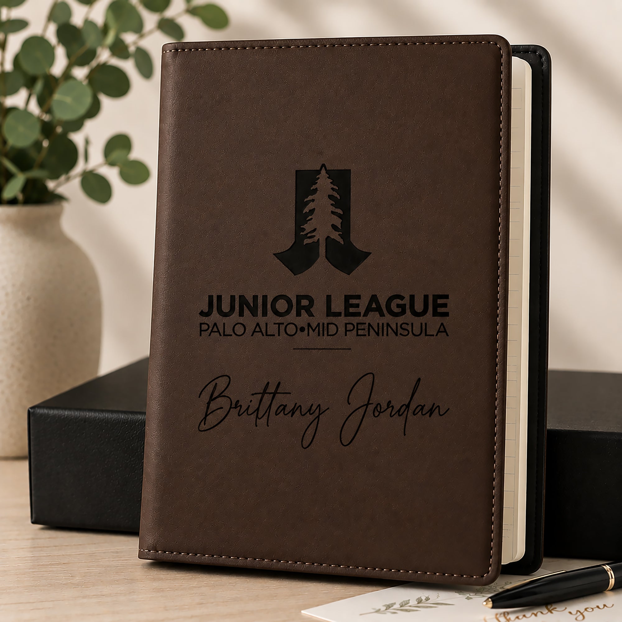 Brown notebook with engraved text and logo on a wooden surface