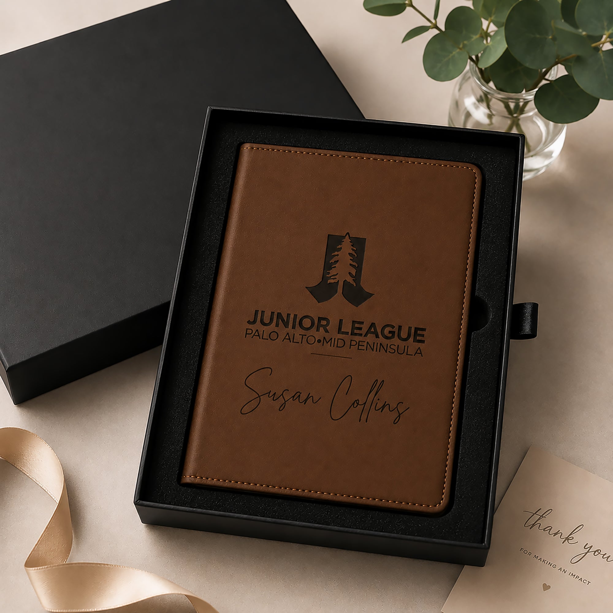 Brown leather notebook with engraved text in a black box on a light surface.