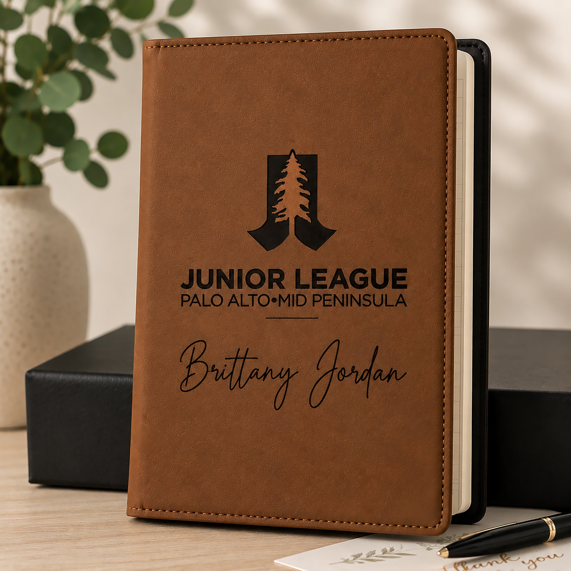 Brown notebook with engraved text and logo on a wooden surface