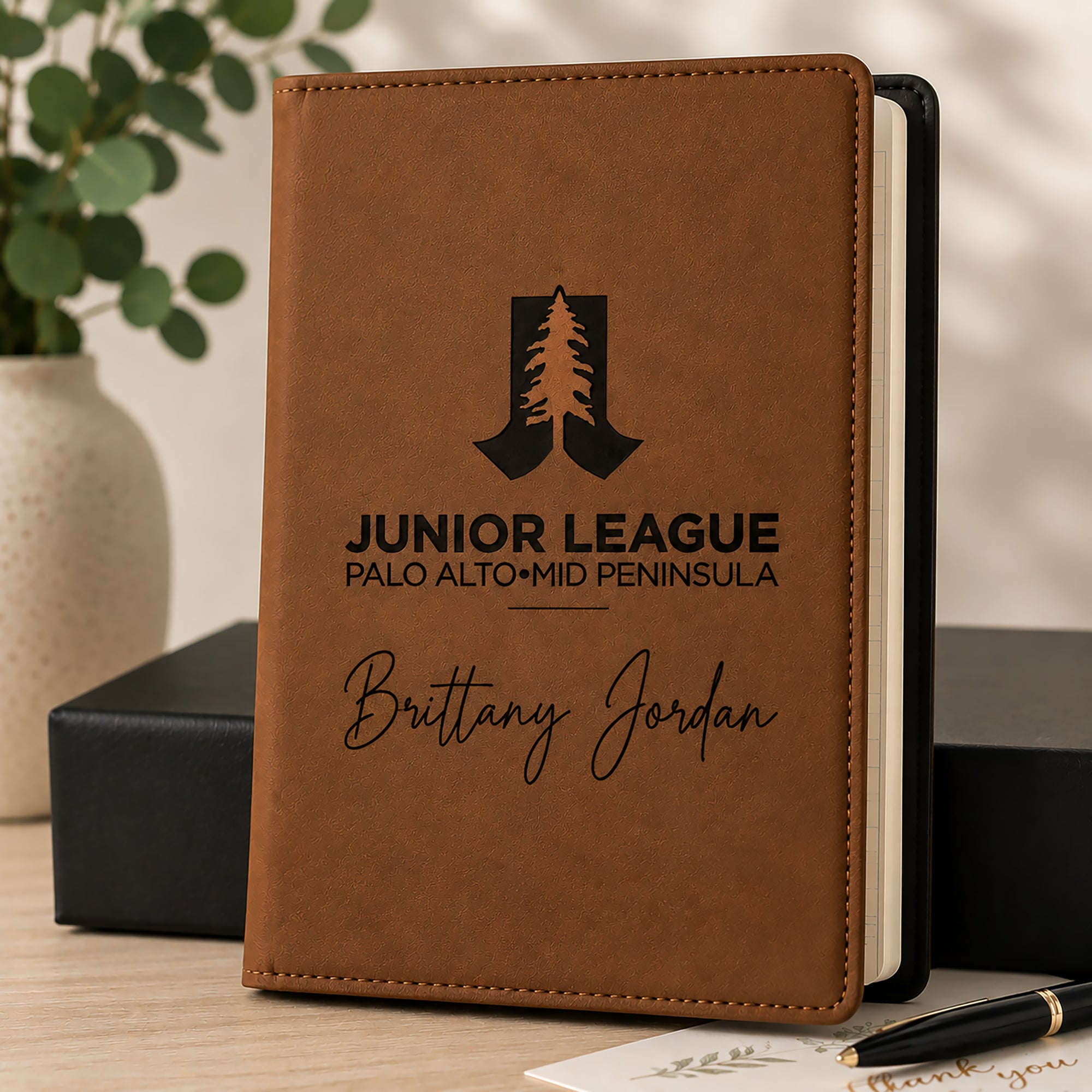 Brown notebook with engraved text and logo on a wooden surface