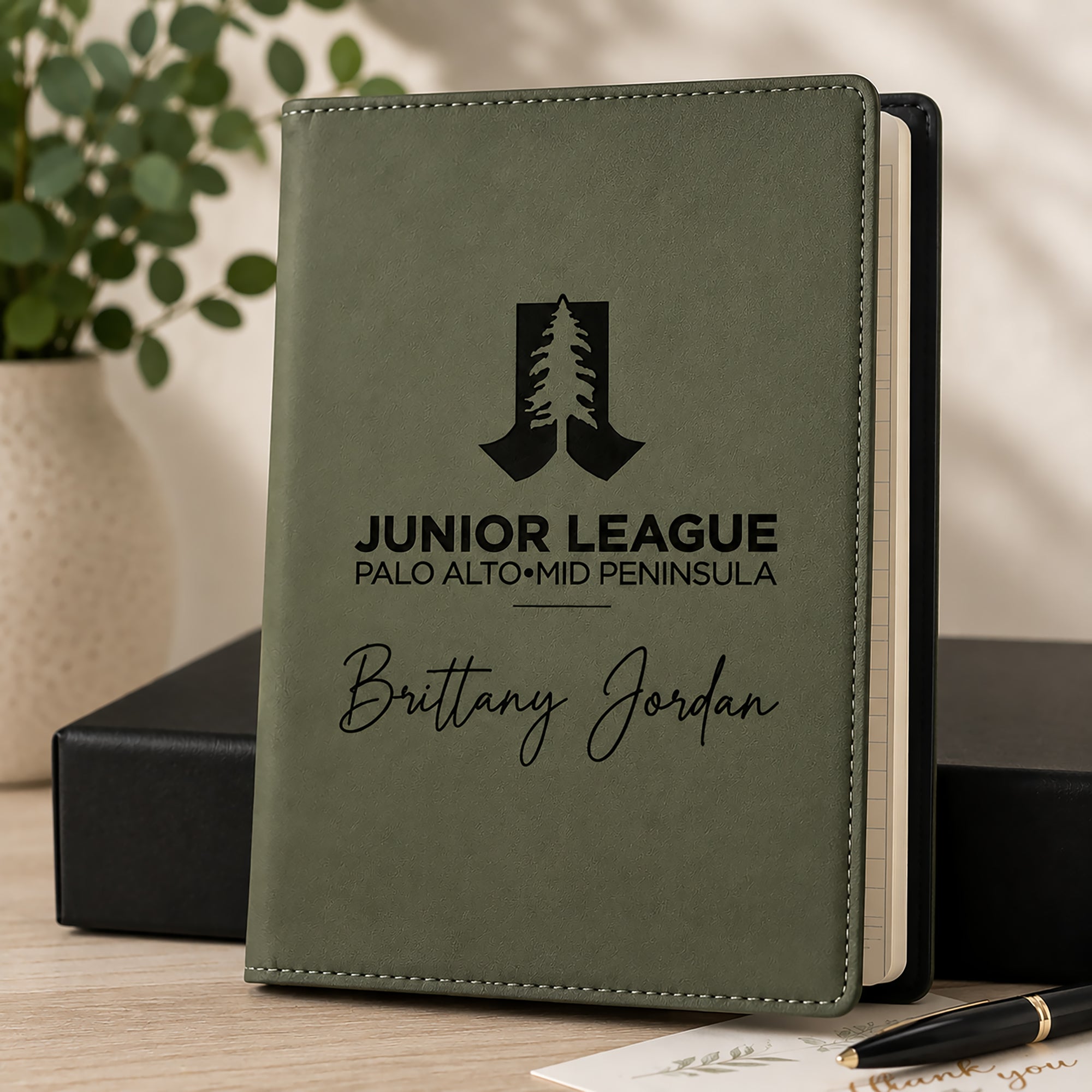Green notebook with engraved text and logo on a wooden surface