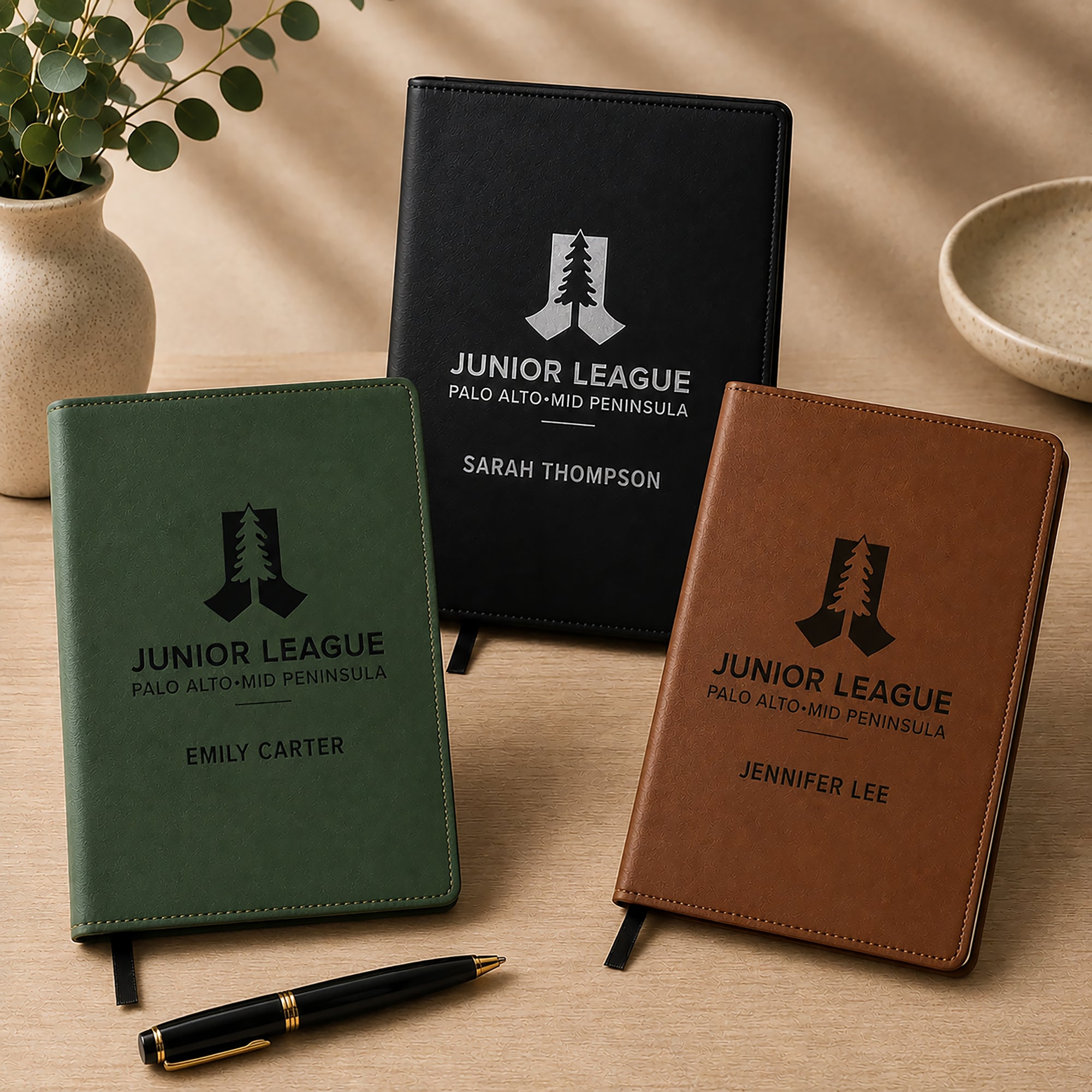 Three personalized notebooks with 'Junior League' branding on a wooden surface.