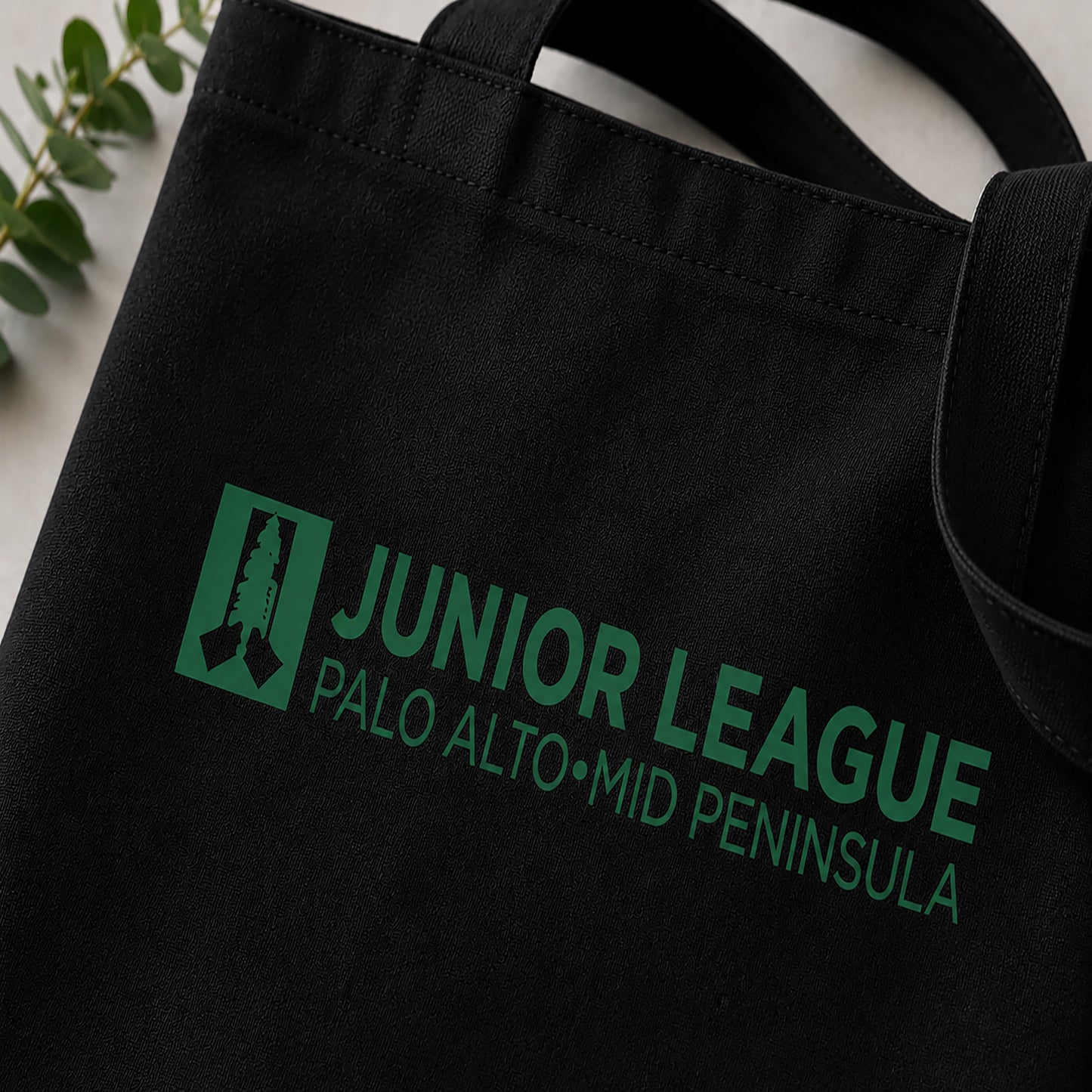 Black tote bag with green 'Junior League Palo Alto Mid Peninsula' text and logo.