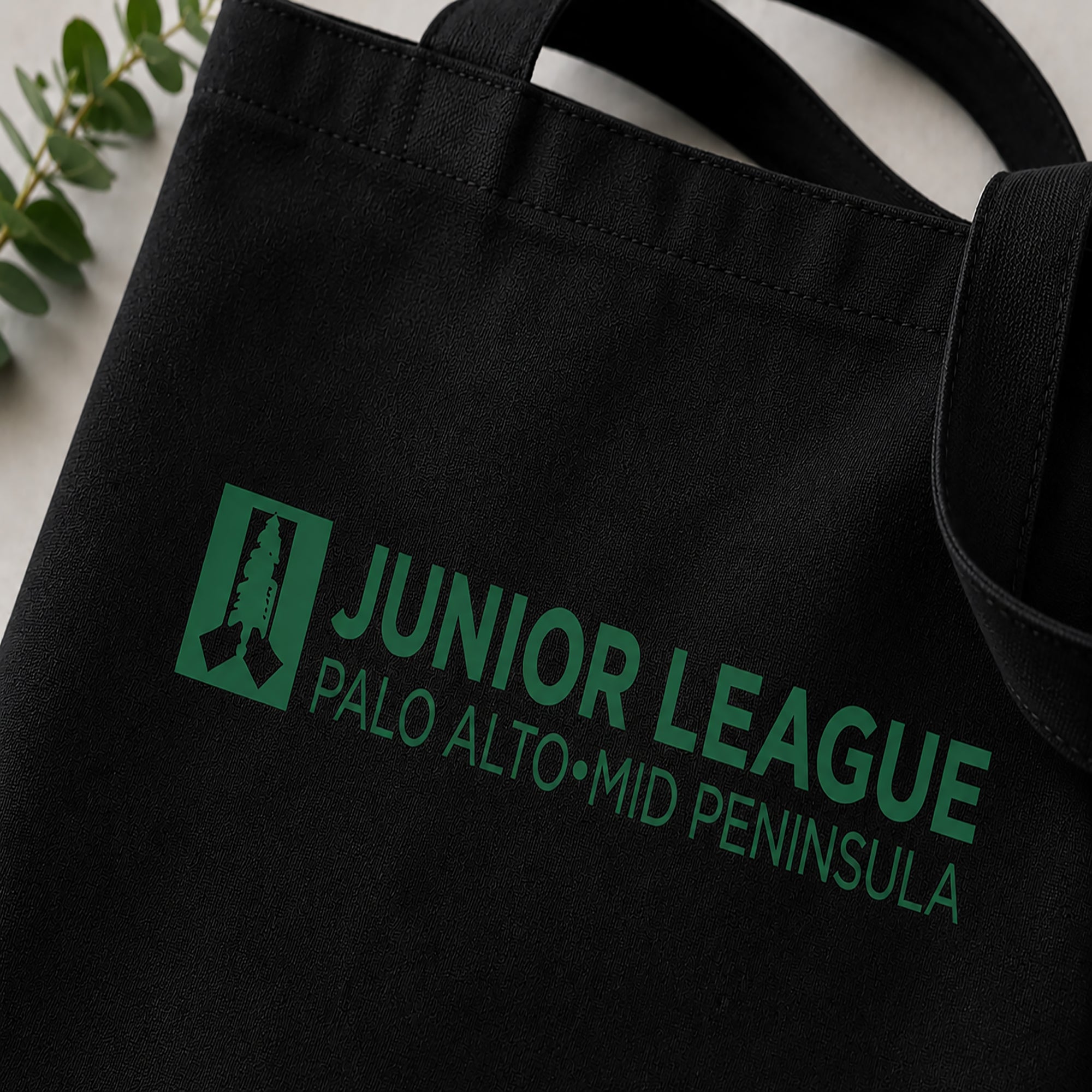 Black tote bag with green 'Junior League Palo Alto Mid Peninsula' text and logo.