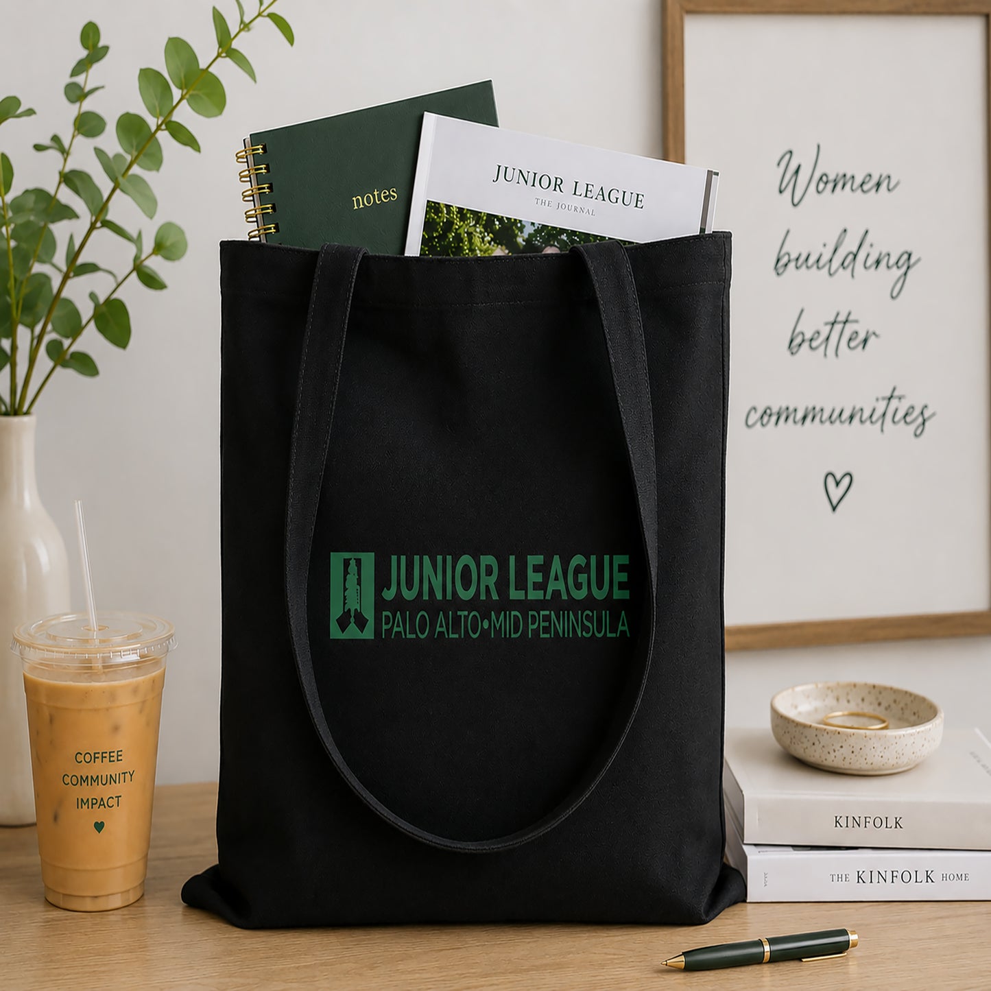 Black tote bag with Junior League logo on a table with a plant and books in the background