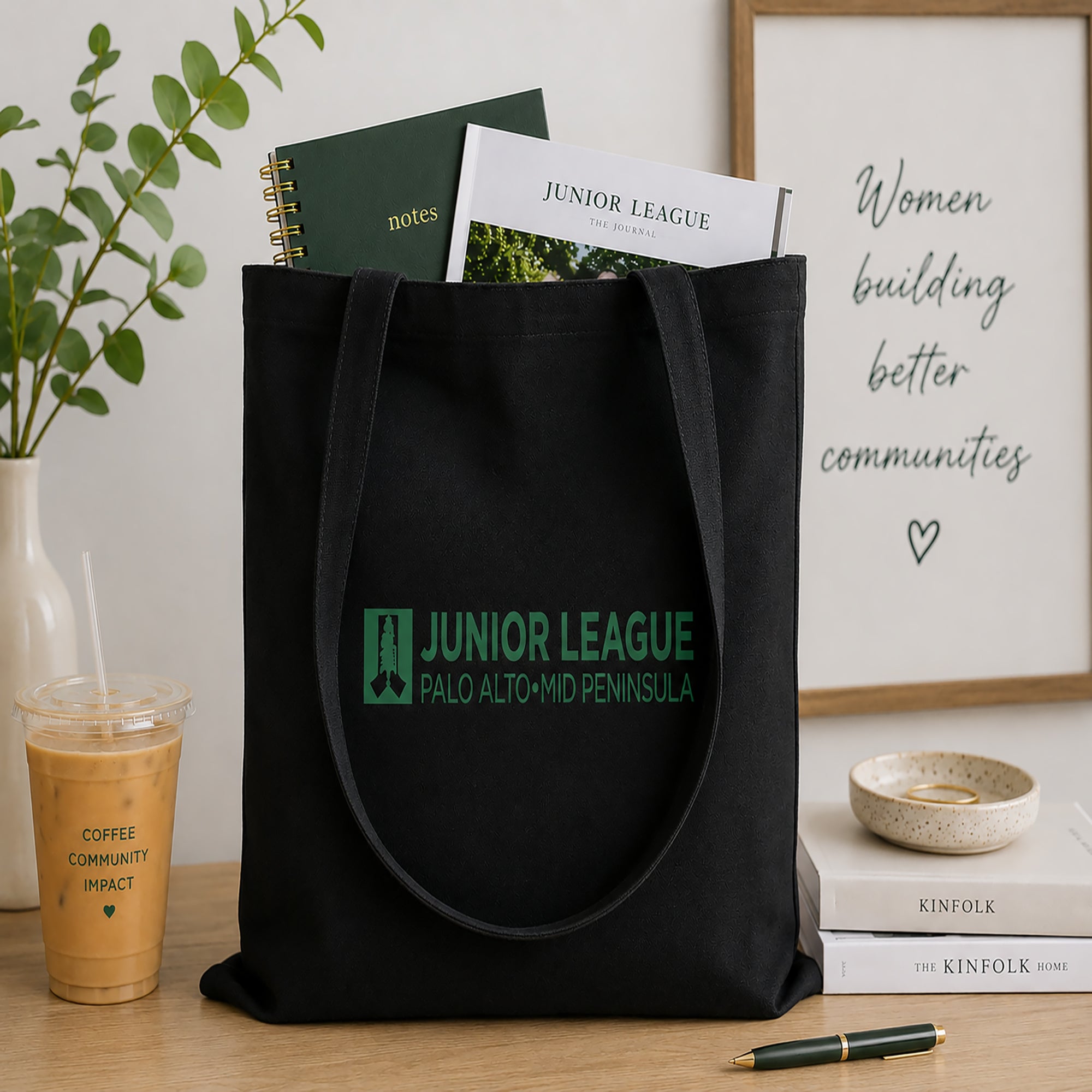 Black tote bag with Junior League logo on a table with a plant and books in the background