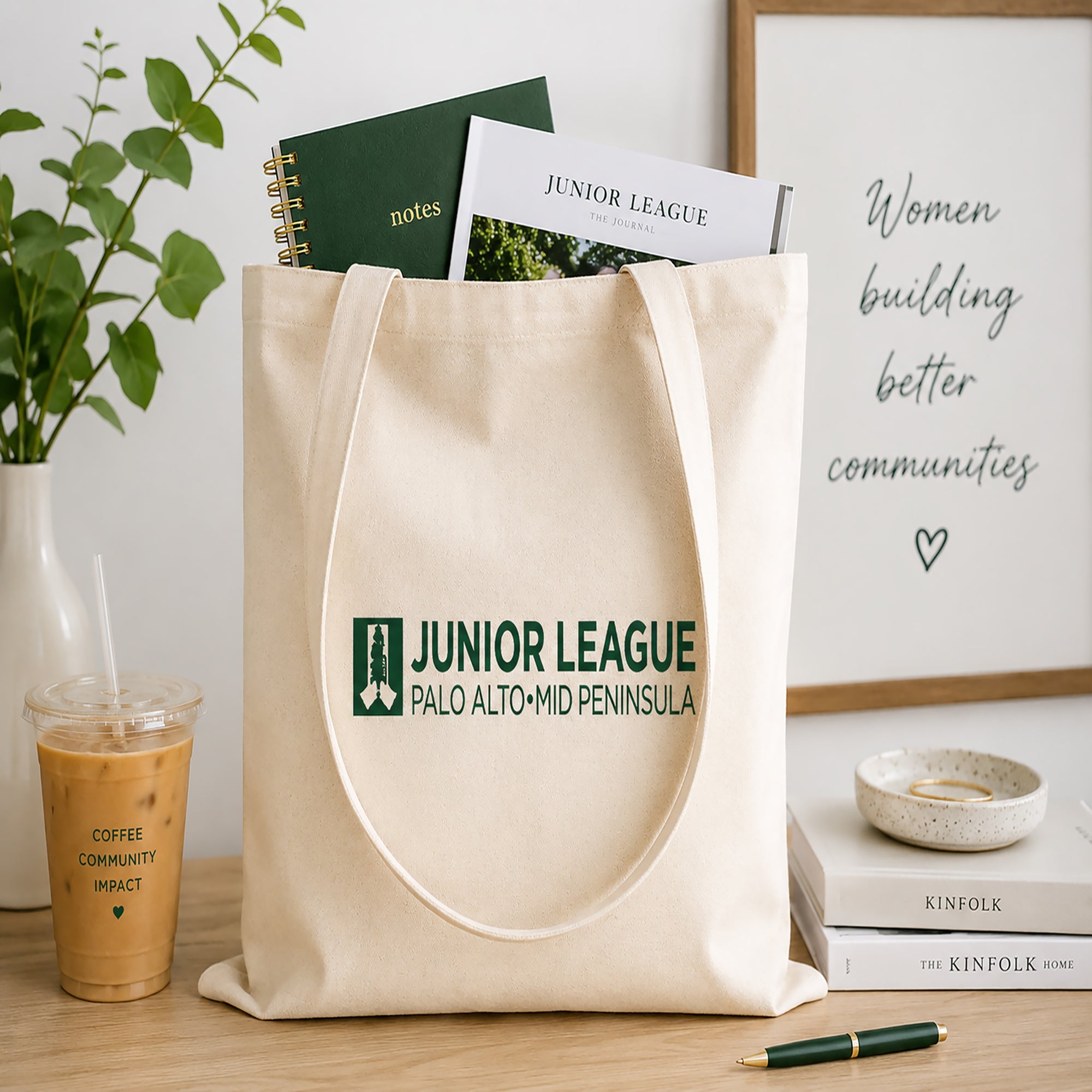 Natural tote bag with Junior League logo on a wooden surface with books and a drink.