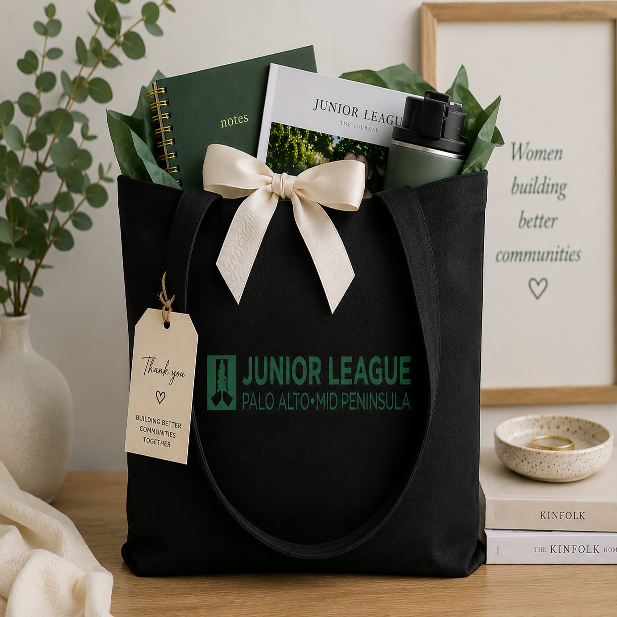 Black tote bag with Junior League Palo Alto/Mid Peninsula branding, filled with stationery items on a wooden surface.