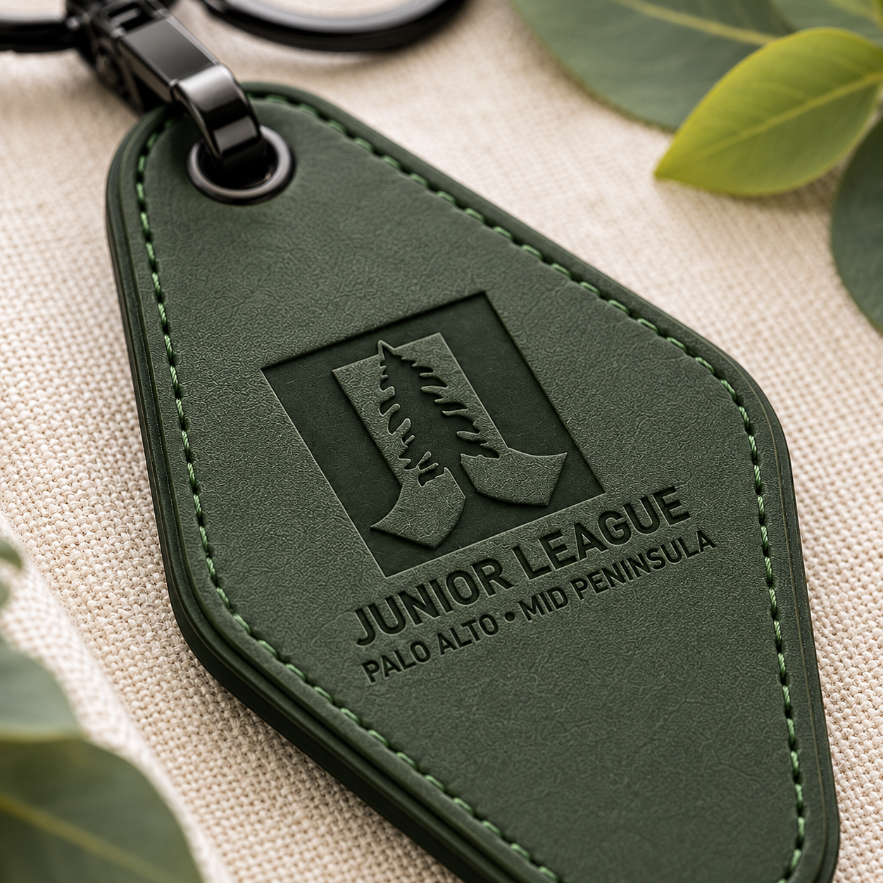 Macro close-up of laser engraved Junior League logo on green vegan leather motel keychain with detailed stitching