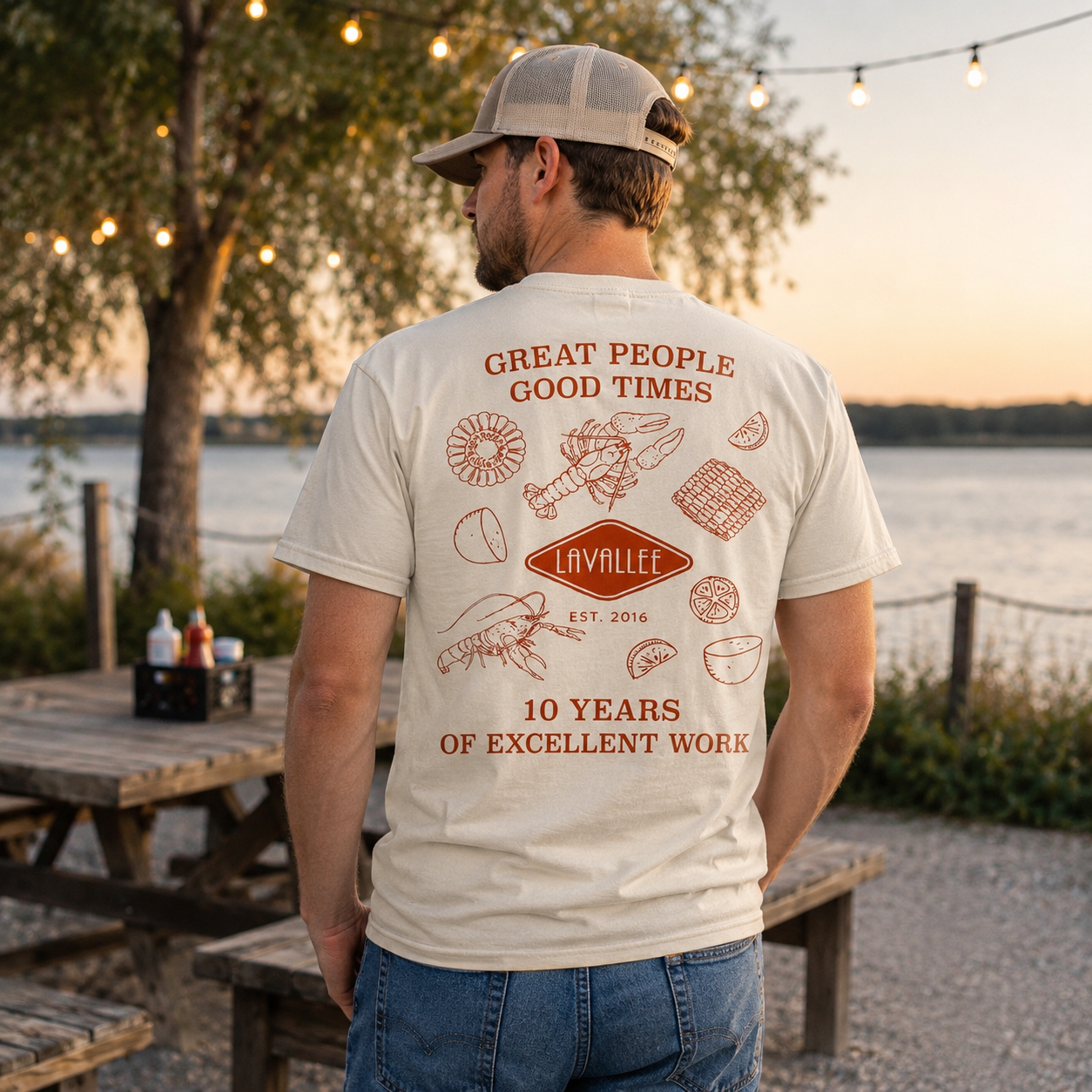Man wearing Lavallee 10-year anniversary company t-shirt outdoors by the water at sunset featuring crawfish boil inspired artwork and vintage Southern lifestyle design.