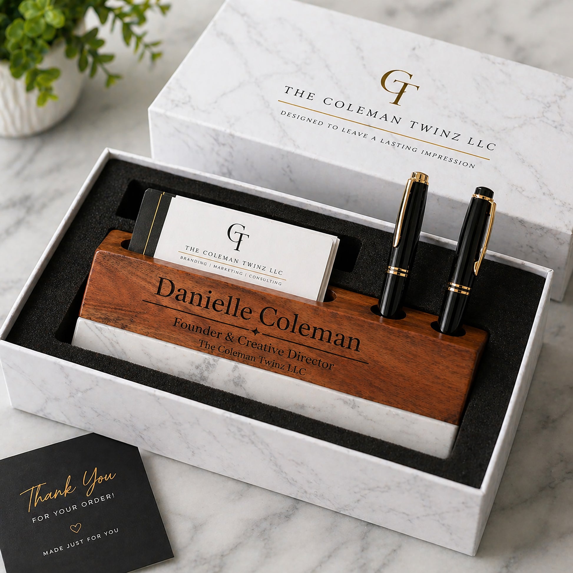 Business card holder with pens and personalized card in a branded box on a marble surface.