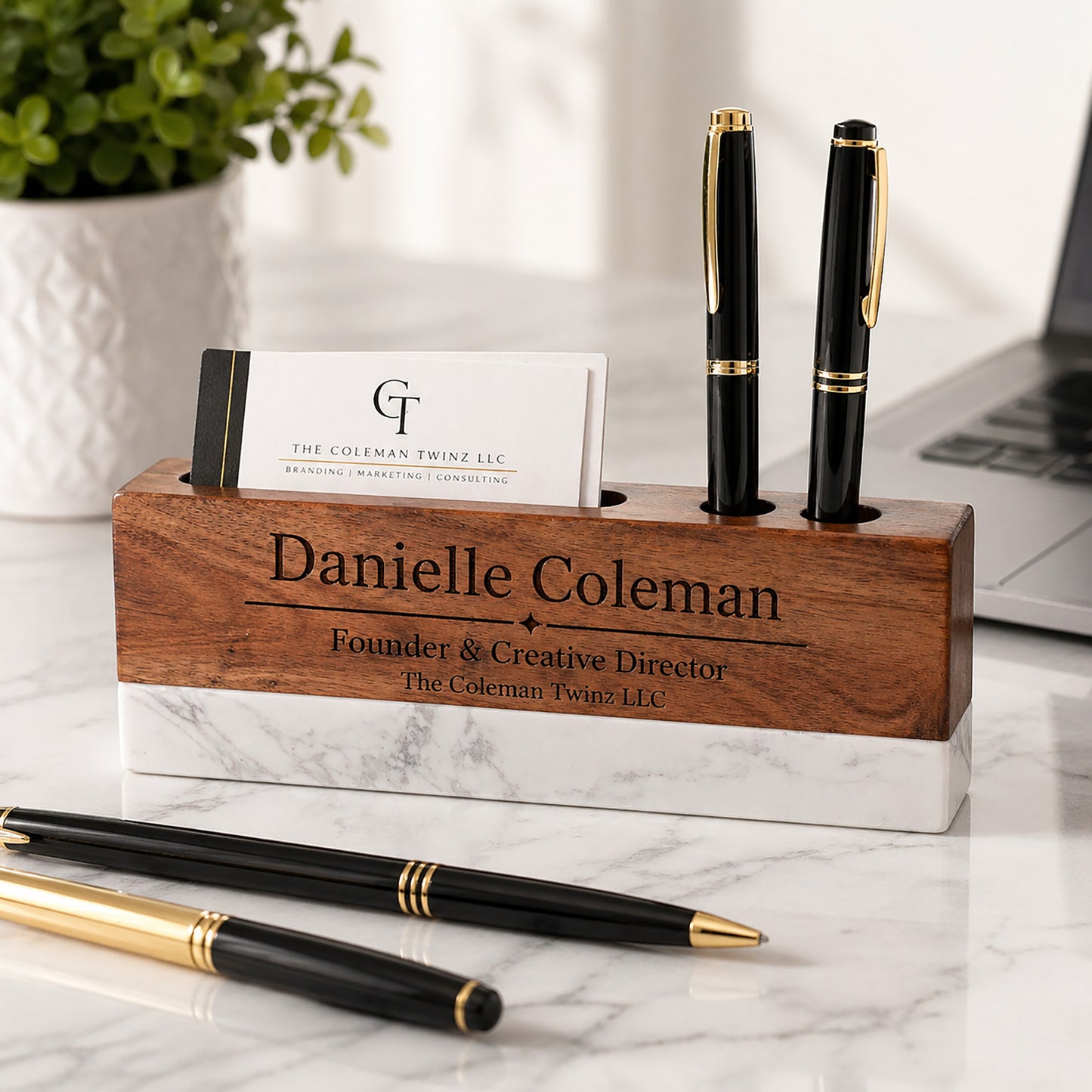 Wooden pen holder with personalized engraving on a marble surface with pens and a laptop in the background.