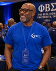 Man wearing a blue Phi Beta Sigma t-shirt with a lanyard, standing in front of a Phi Beta Sigma banner.