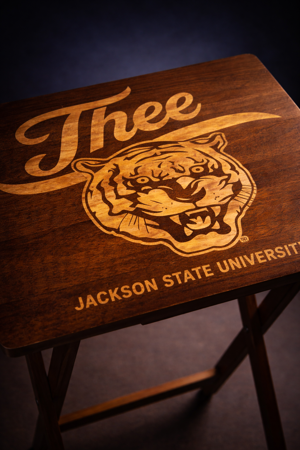 Close-up of dark wood folding tray table with engraved tiger crest and Jackson State University