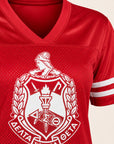 A close-up of a red mesh V-neck athletic jersey with a large white fraternity-style crest printed on the front and white sleeve stripes.