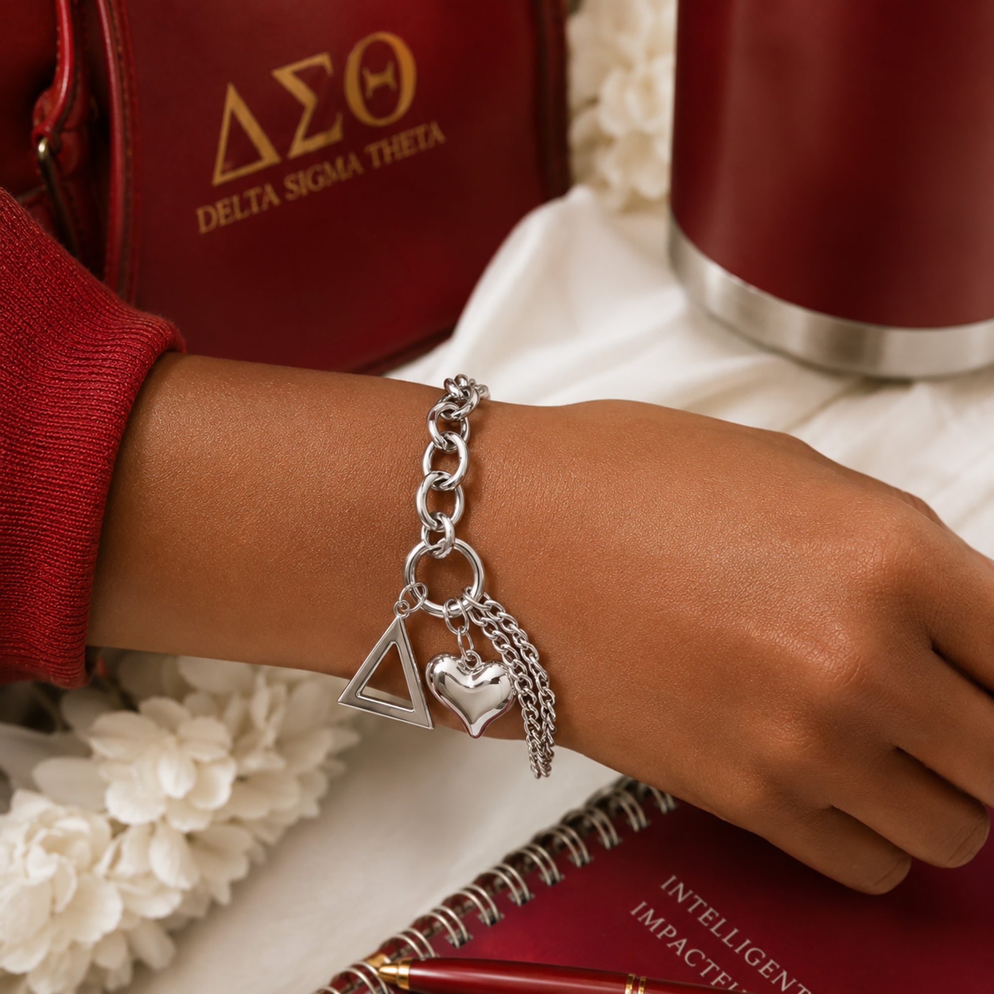 Close-up of Delta Sigma Theta pyramid charm bracelet worn on wrist with matching sorority accessories in crimson and gold.
